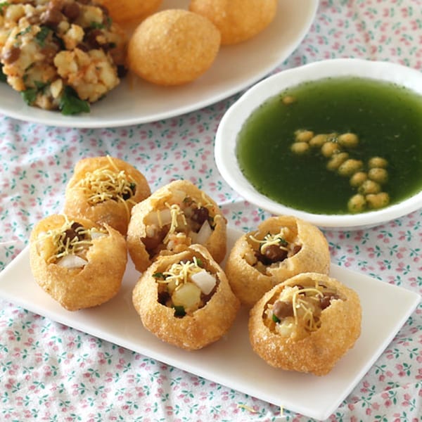A plate of pani puri, filled with potatoes and chickpeas, next to a bowl of green pani.