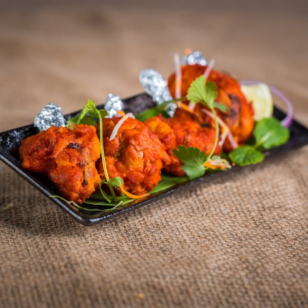 Bawarchi Biryanis' Indian chicken lollipops, garnished with cilantro and lemon, on a black plate.