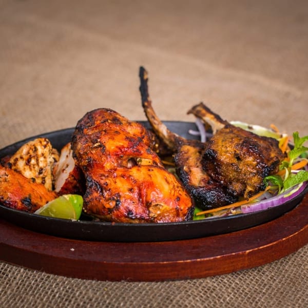 Sizzling Indian tandoori chicken and lamb chops with lime and onions on a black platter.