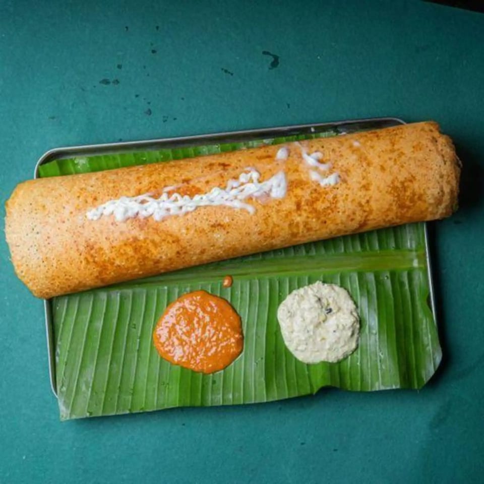 A golden-brown dosa with white sauce, served on a banana leaf with two chutneys.