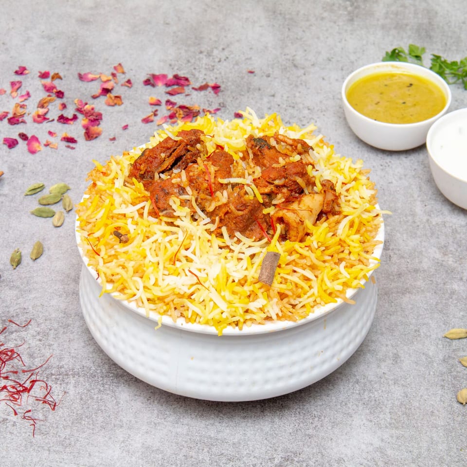 A white bowl of Bawarchi Biryanis' chicken biryani with yellow rice, spices, and two side sauces.