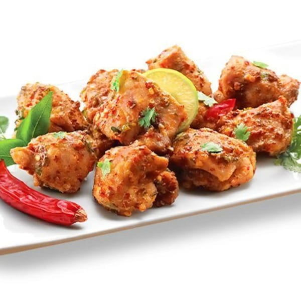 Spicy Indian chicken appetizer, garnished with lime, chili, and fresh herbs on a white plate.