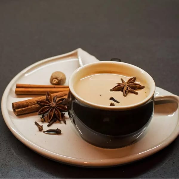 Indian chai tea in a black cup with star anise, cinnamon sticks, and cloves on a white plate.