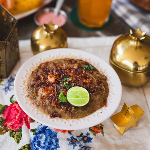 A plate of Indian Haleem, garnished with fried onions, cilantro, and a lime wedge.