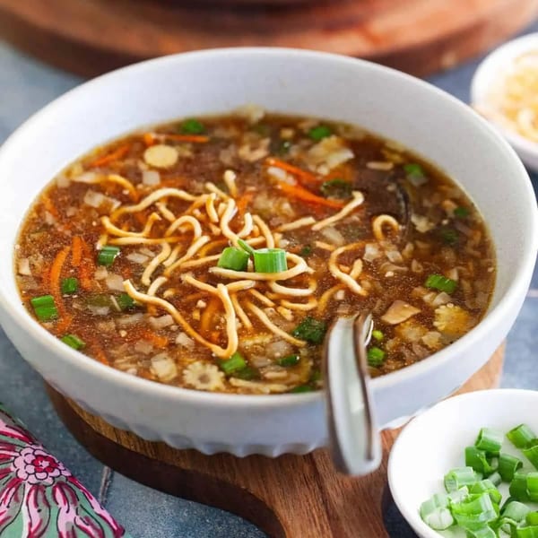 A white bowl of Indian hot and sour soup with noodles, carrots, and green onions.