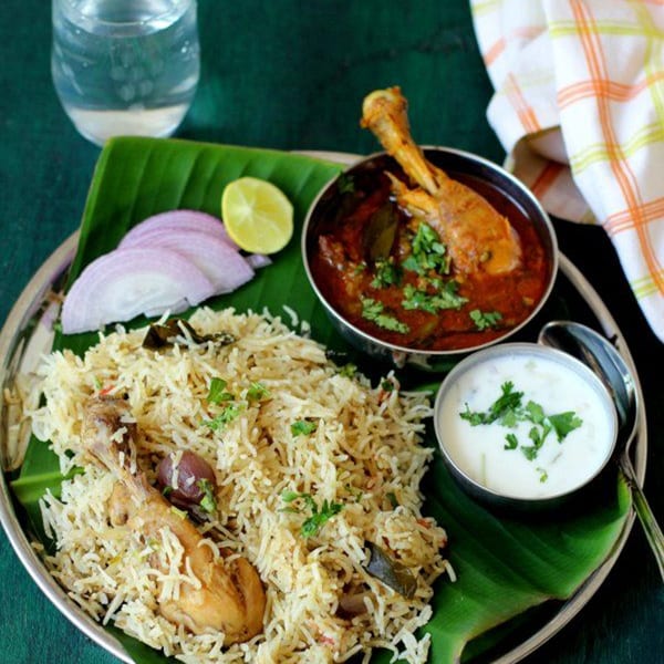Bawarchi Biryanis' chicken biryani with raita, curry, onions, and lime on a banana leaf.